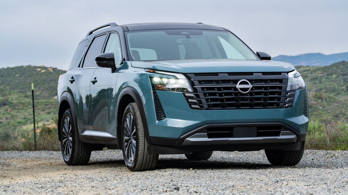 A 2026 Nissan Pathfinder Platinum with its headlights on in a front right-side 3/4 view against a green background with cloudy skies.