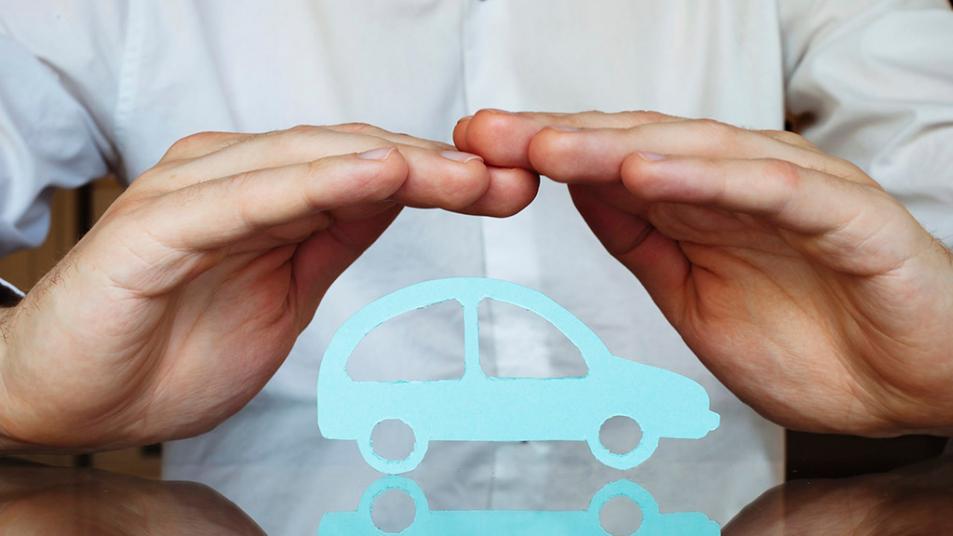 A person's hands form an arch over a paper car.