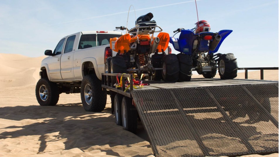 ATVs on a trailer behind lifted pickup truck