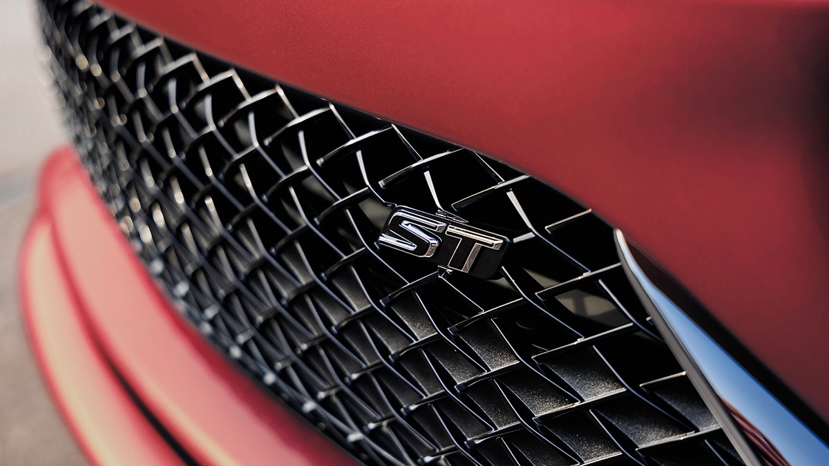 Close-up view of grille and badge of the 2024 Buick Envista ST in Sunrise Red Metallic. Preproduction model shown. Actual production model may vary. Available in summer 2023.